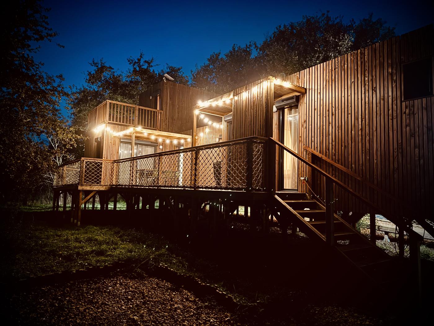 Aloudi House le soir, maison en bois sur pilotis éclairée de guirlandes